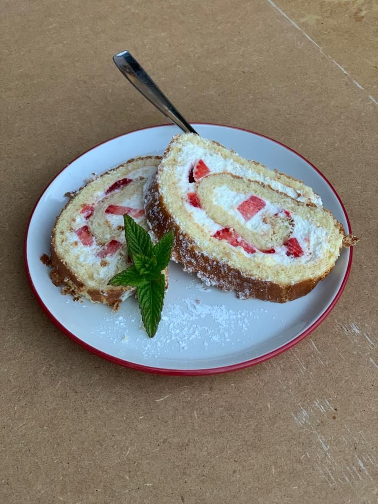 Una porción de bizcocho relleno de fresa y crema sobre un plato blanco con borde rojo, decorado con una hoja de menta.