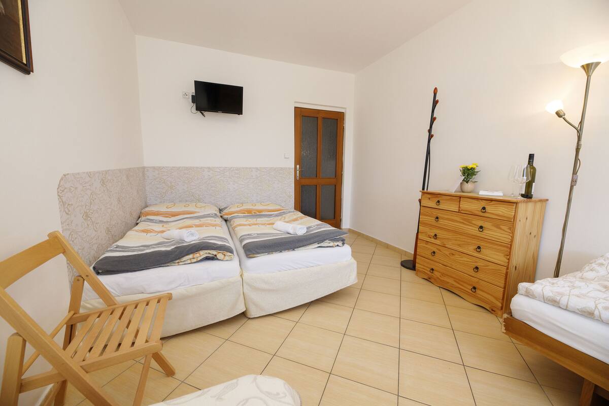 A bedroom with a bed, a wooden dresser, a TV mounted on the wall, and a chair.