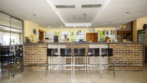 A modern bar area with a brick wall, metal chairs, and a counter with various bottles and decorations. - Hotel Vintíř (Hartmanice)