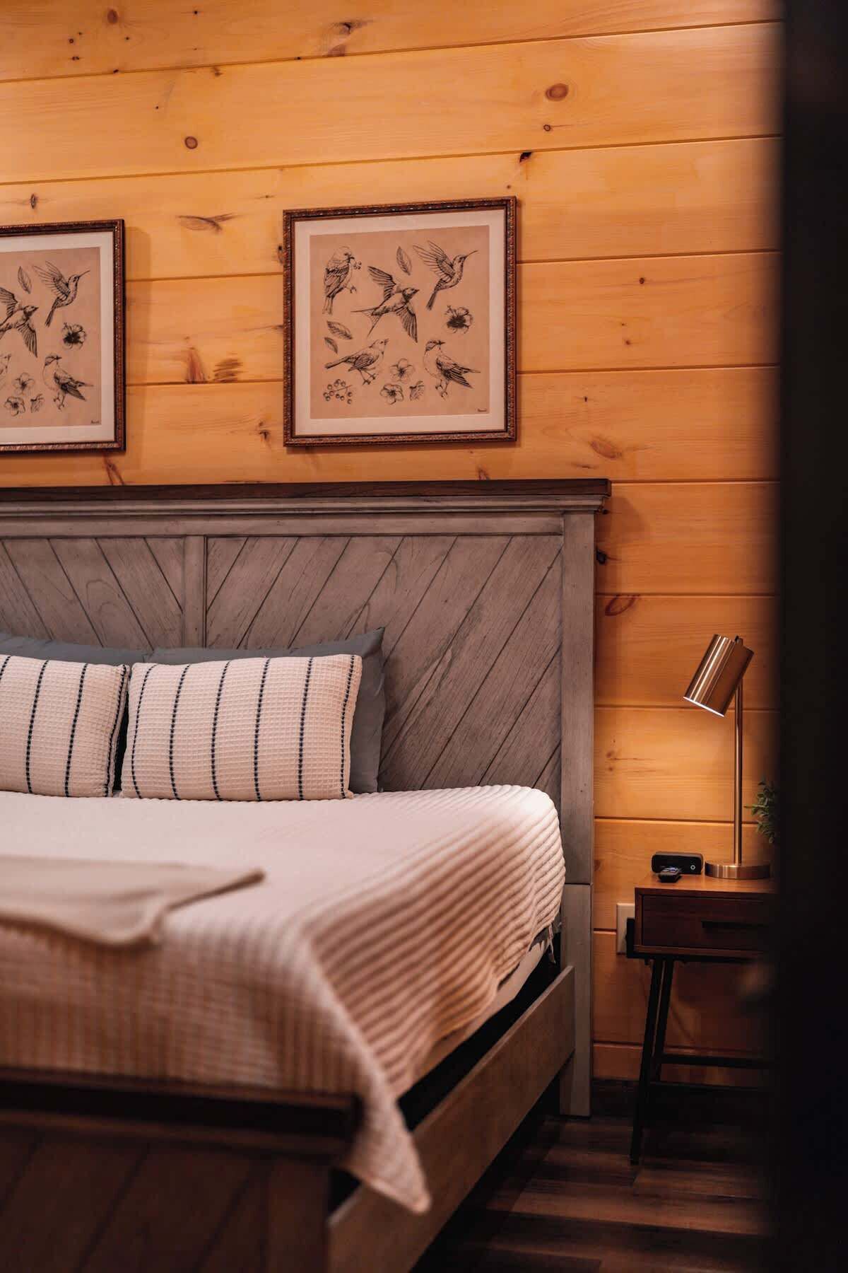 A bedroom with a wooden headboard, a bed with striped pillows, and two framed bird illustrations on the wall.