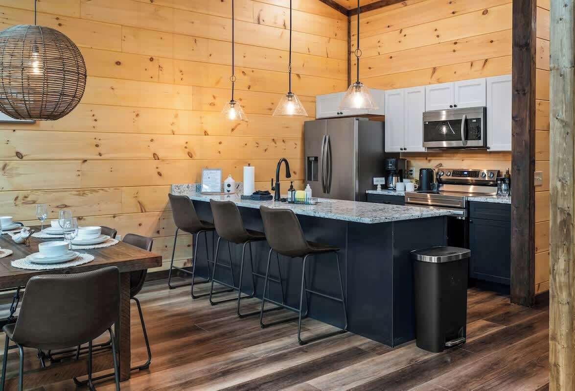 A modern kitchen with wooden walls, a central island with bar stools, stainless steel appliances, and pendant lighting.