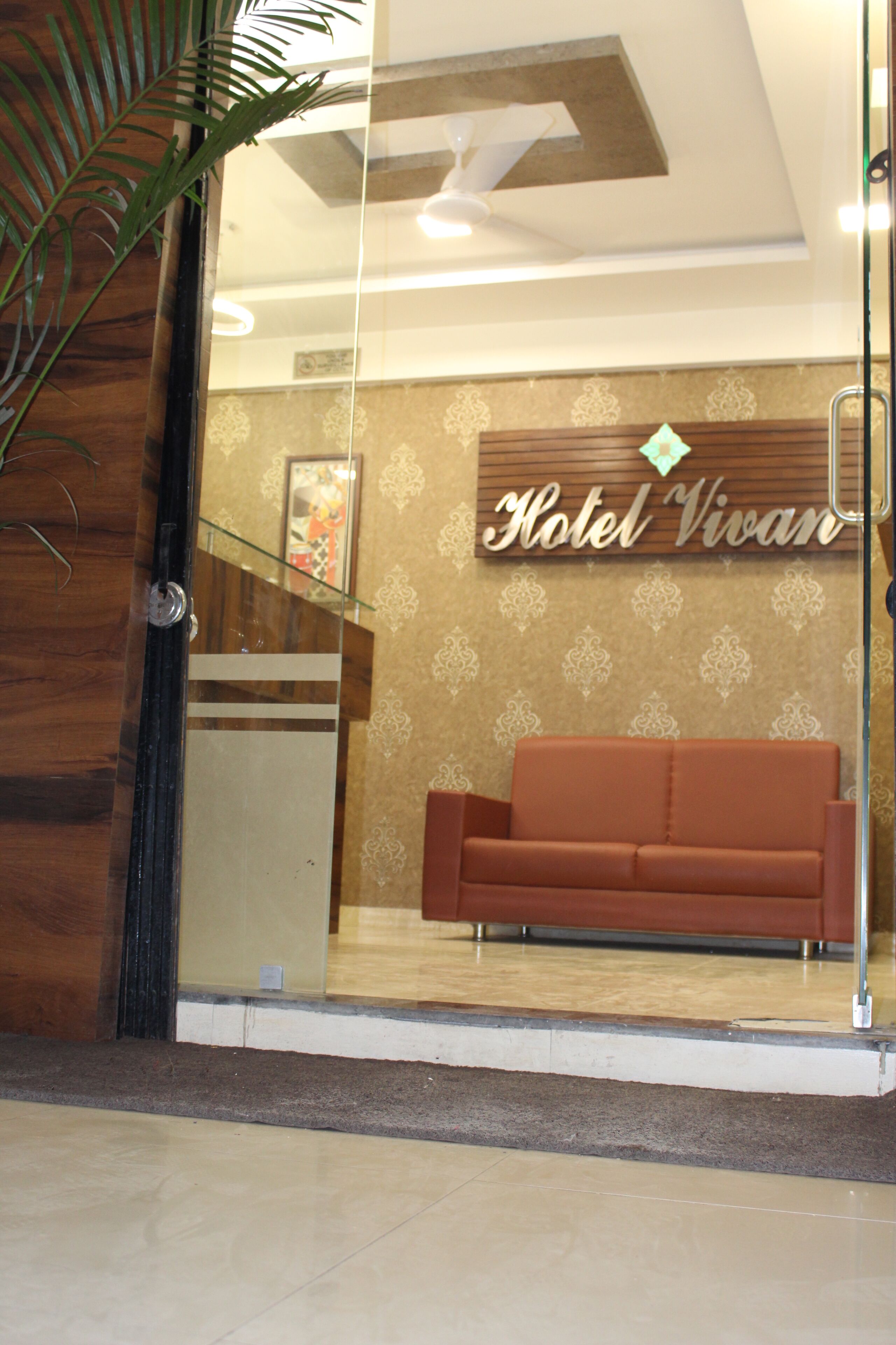 A reception area with a brown sofa, a glass partition, and a ceiling fan.