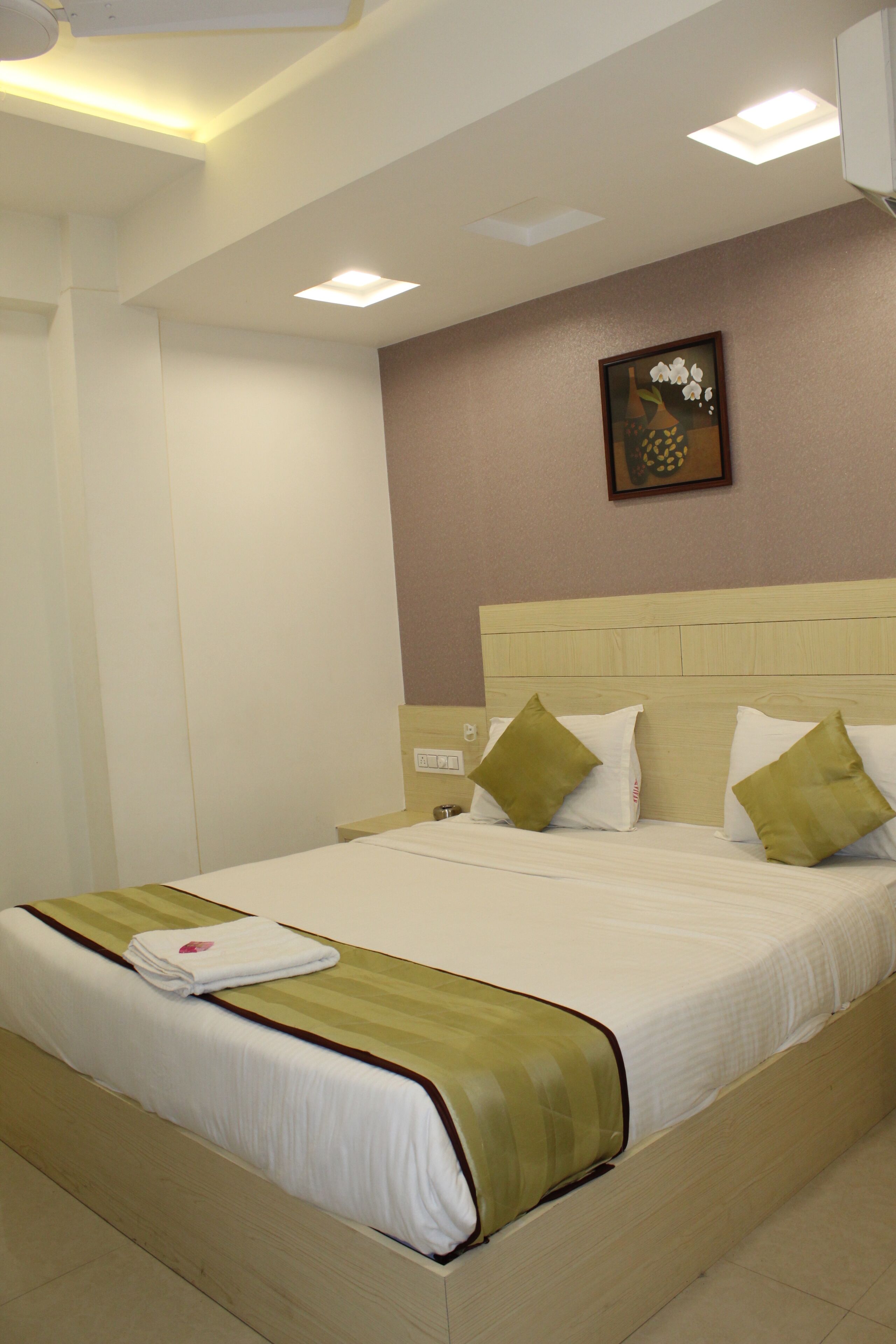 A neatly made bed with a white and green bedspread, a single pillow, and a folded towel on the side.
