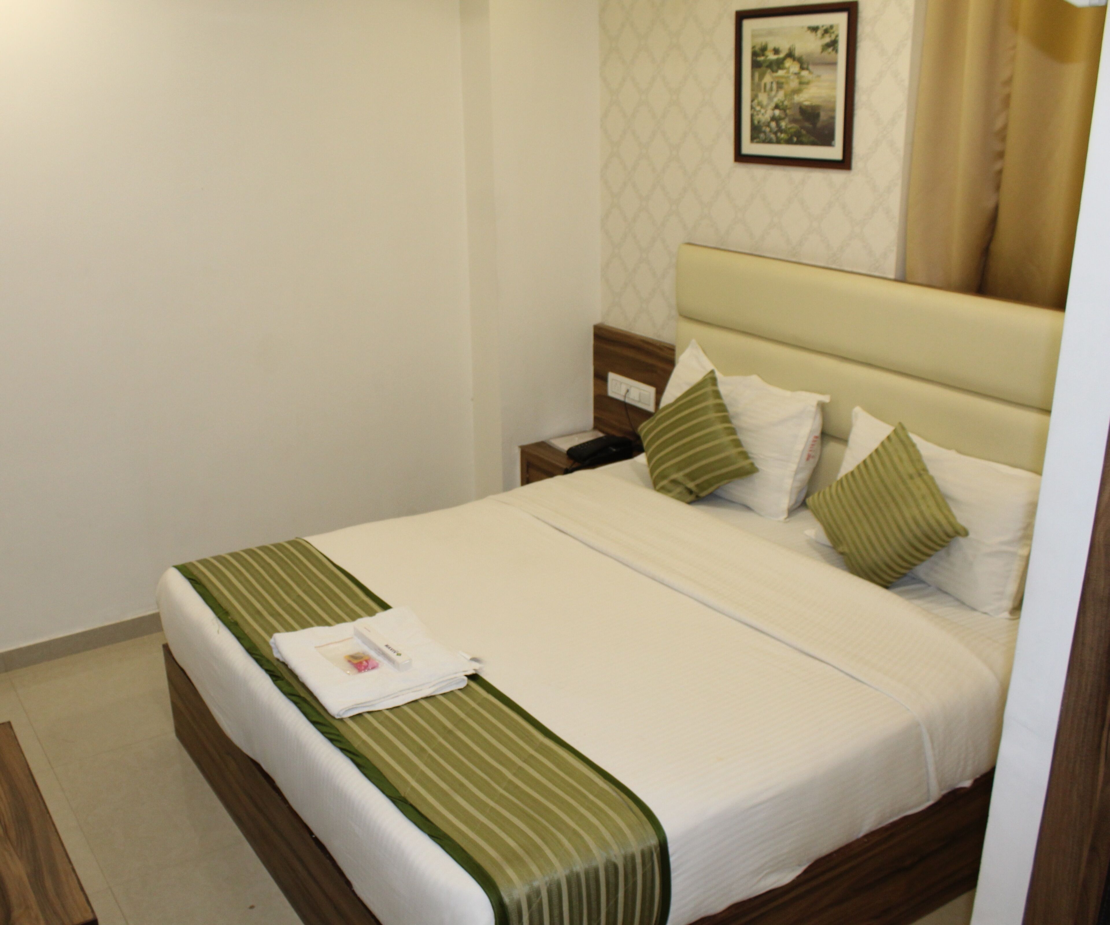 A neatly made bed with a striped bedspread, two pillows, and a bedside table with a phone and a small item on it.