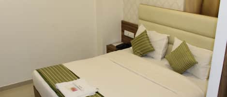A neatly made bed with a striped bedspread, two pillows, and a bedside table with a phone and a small item on it.