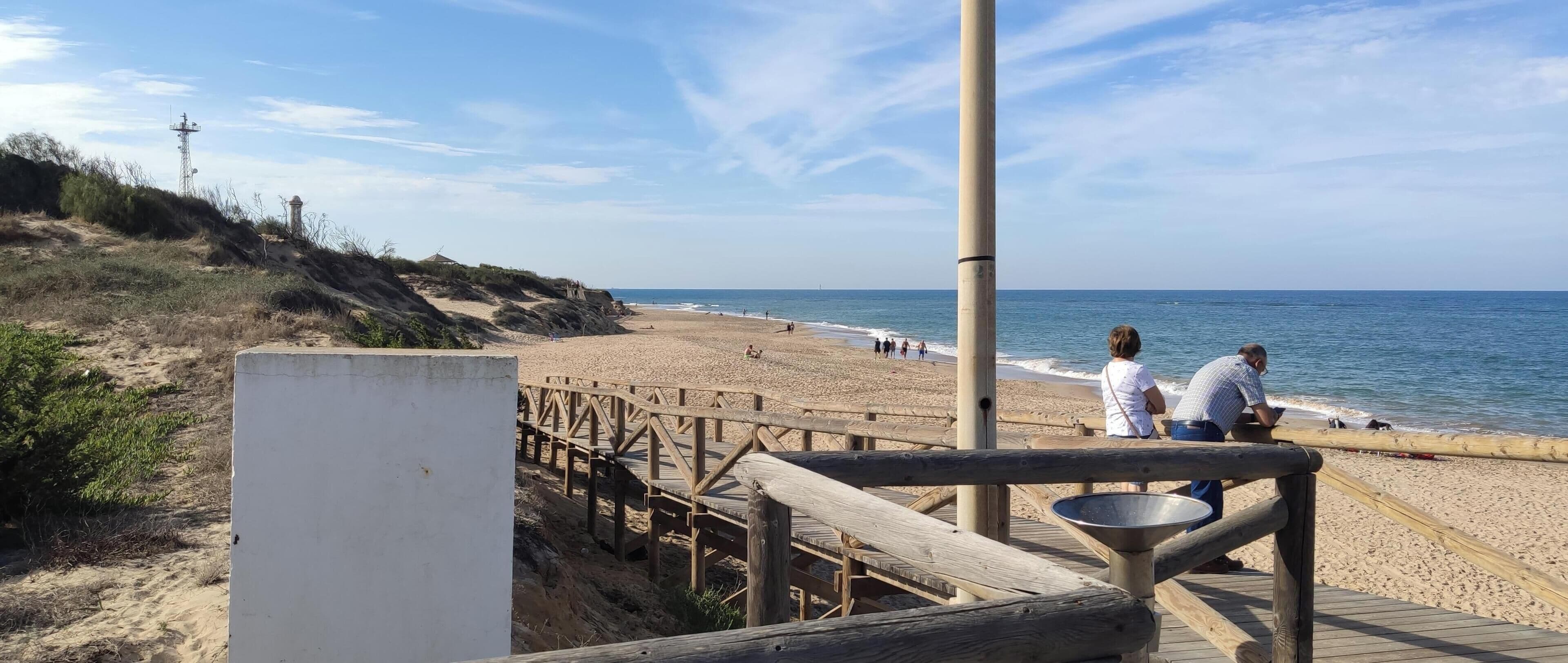 Una pasarela de madera que lleva a una playa arenosa bajo un cielo despejado.