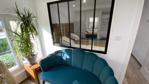 Ein modernes Wohnzimmer mit einem blaugrünen Sofa, einem großen Fenster und einer Topfpflanze.