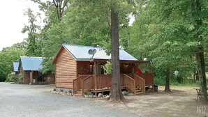 A rustic cabin with a porch and a satellite dish, surrounded by trees.