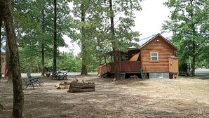 A rustic cabin with a deck, surrounded by trees.
