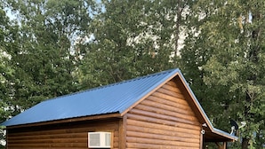 A log cabin with a blue metal roof, a small porch, and a gravel driveway.