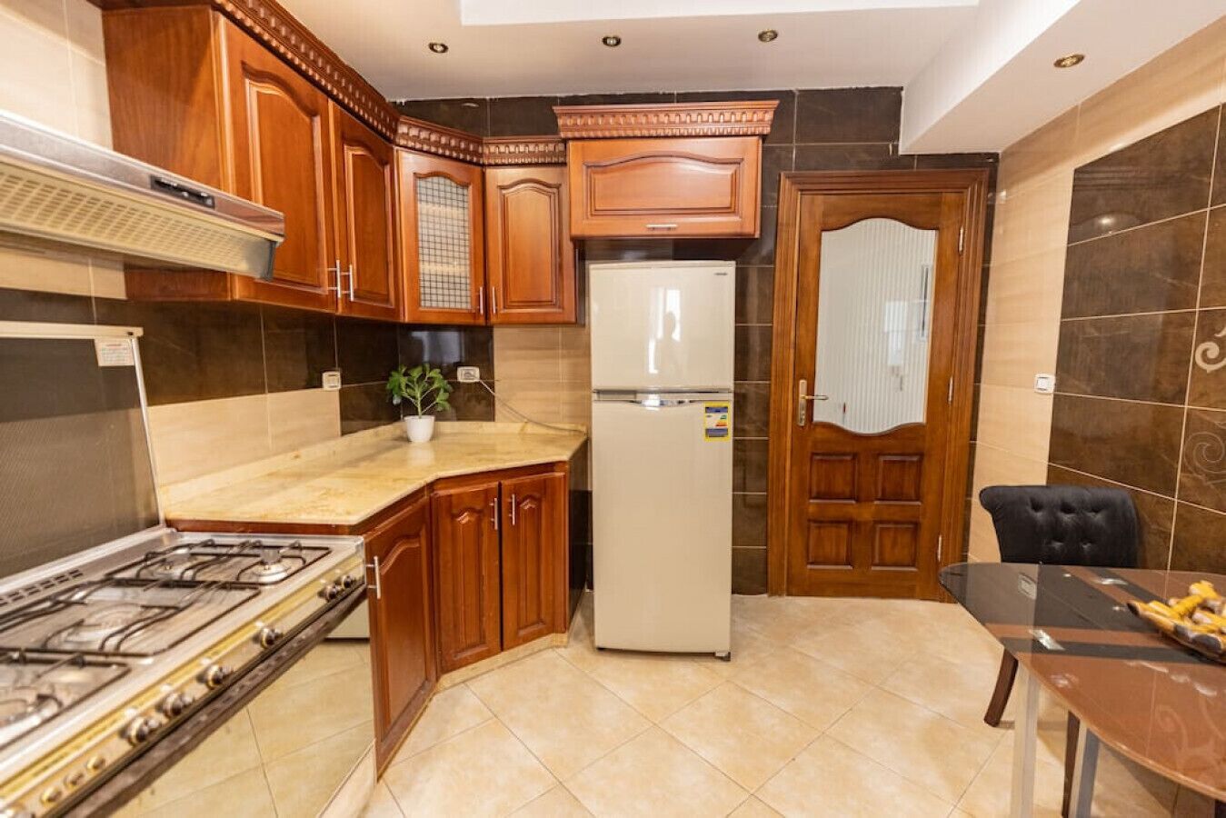 Une cuisine avec des meubles de rangement en bois, une cuisinière à gaz, un réfrigérateur et une table à manger avec des chaises.