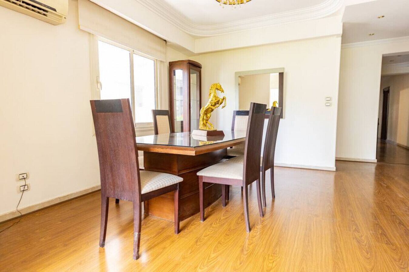 Ein Essbereich mit Holztisch und -stühlen, einem großen Spiegel und einer goldenen Skulptur eines Pferdes.