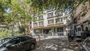 Un immeuble à plusieurs étages, doté d’une entrée centrale, entouré de voitures garées et d’arbres.