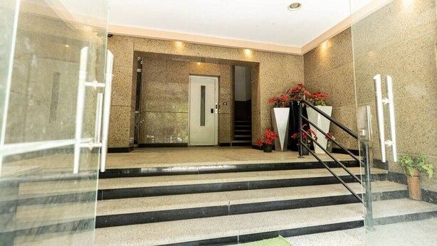 Un hall d’entrée moderne avec une entrée en verre, un escalier et une porte donnant accès à un ascenseur.