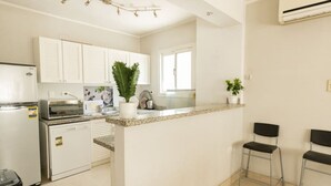 A modern kitchen with white cabinets, a granite countertop, a built-in oven, and a small island with bar stools. - Lily Mint Comfy 3BR W/Sitting room TV Apartment (Maadi as Sarayat Al Gharbeyah)