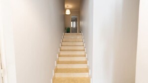 A narrow, light-colored hallway with a wooden staircase leading to a door at the end. - Lily Mint Comfy 3BR W/Sitting room TV Apartment (Maadi as Sarayat Al Gharbeyah)