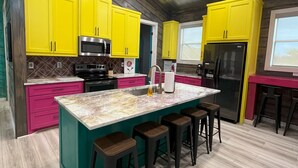 A modern kitchen with yellow cabinets, a marble island, and wooden flooring.