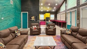 A modern interior with a central seating area, a kitchen in the background, and a high ceiling with linear lighting.