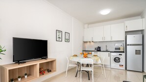 Una cocina moderna con armarios blancos, lavadora integrada, microondas y televisor de pantalla plana sobre un soporte de madera.