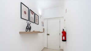 Un pasillo con una puerta blanca, un extintor y un estante con una bicicleta y un libro.