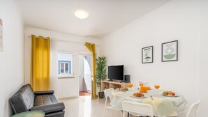 Una sala de estar moderna con un sofá, una mesa de comedor con desayuno, un televisor y obras de arte en la pared.