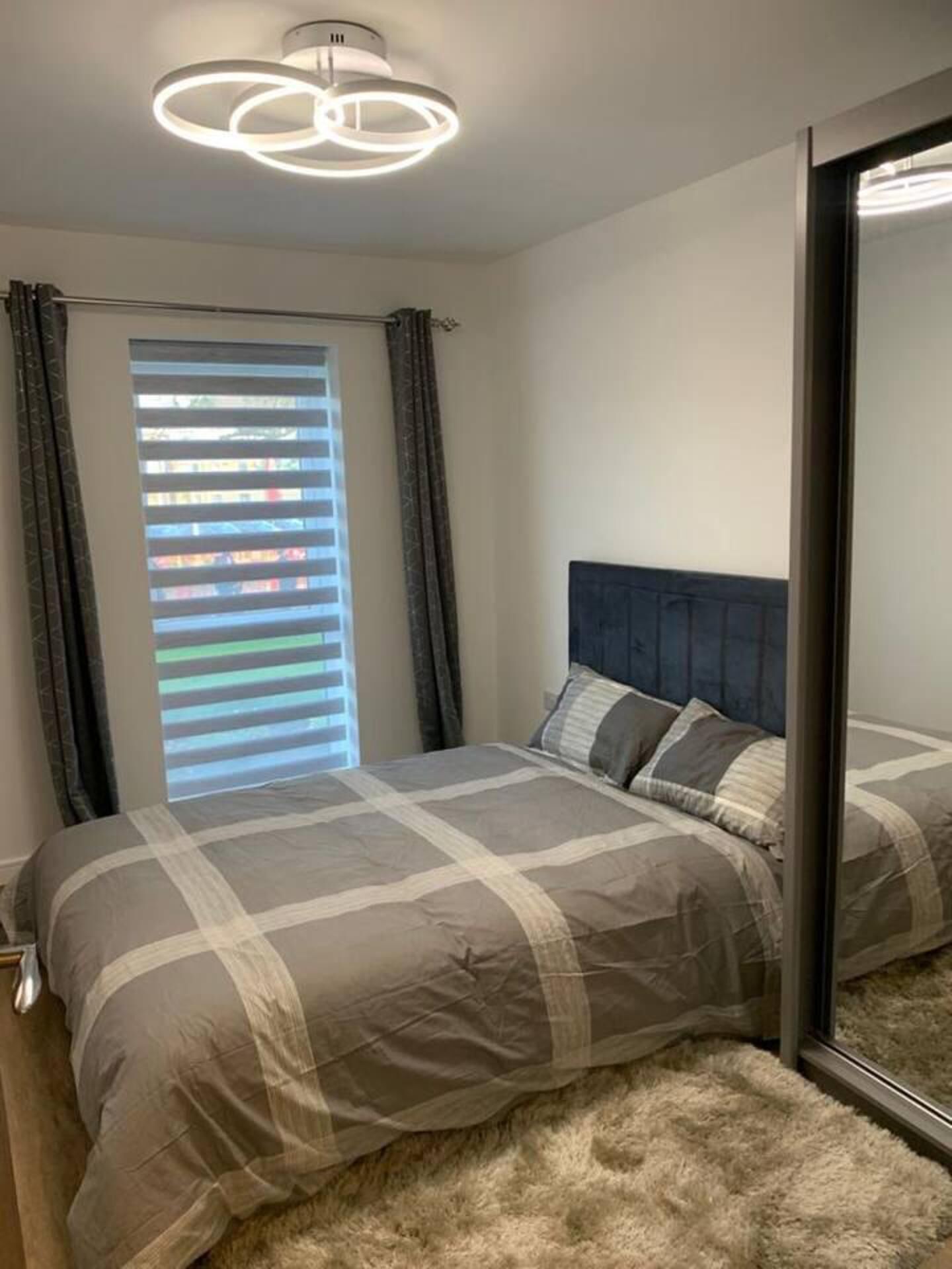 A bedroom with a bed, a window with blinds, and a ceiling light fixture.
