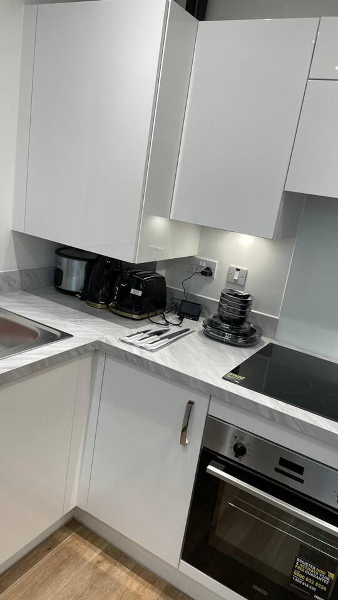A modern kitchen with white cabinets, a built-in oven, a coffee maker, and a kettle on the countertop.
