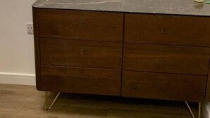 Ein Holzk dresser mit Schubladen, ein kleiner Tisch mit Kerze und ein an der Wand befestigtes Thermostat.