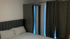 Ein Schlafzimmer mit Bett, Kopfteil, Deckenleuchte und einem Fenster mit Vorhängen.