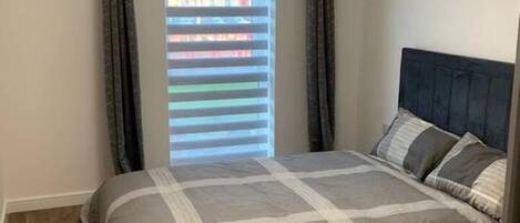A bedroom with a bed, a headboard, a window with blinds, and a ceiling light fixture.