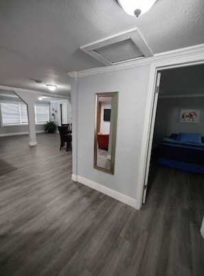 Une pièce spacieuse avec un plancher en bois, un grand miroir et un lit recouvert d’une couverture bleue.