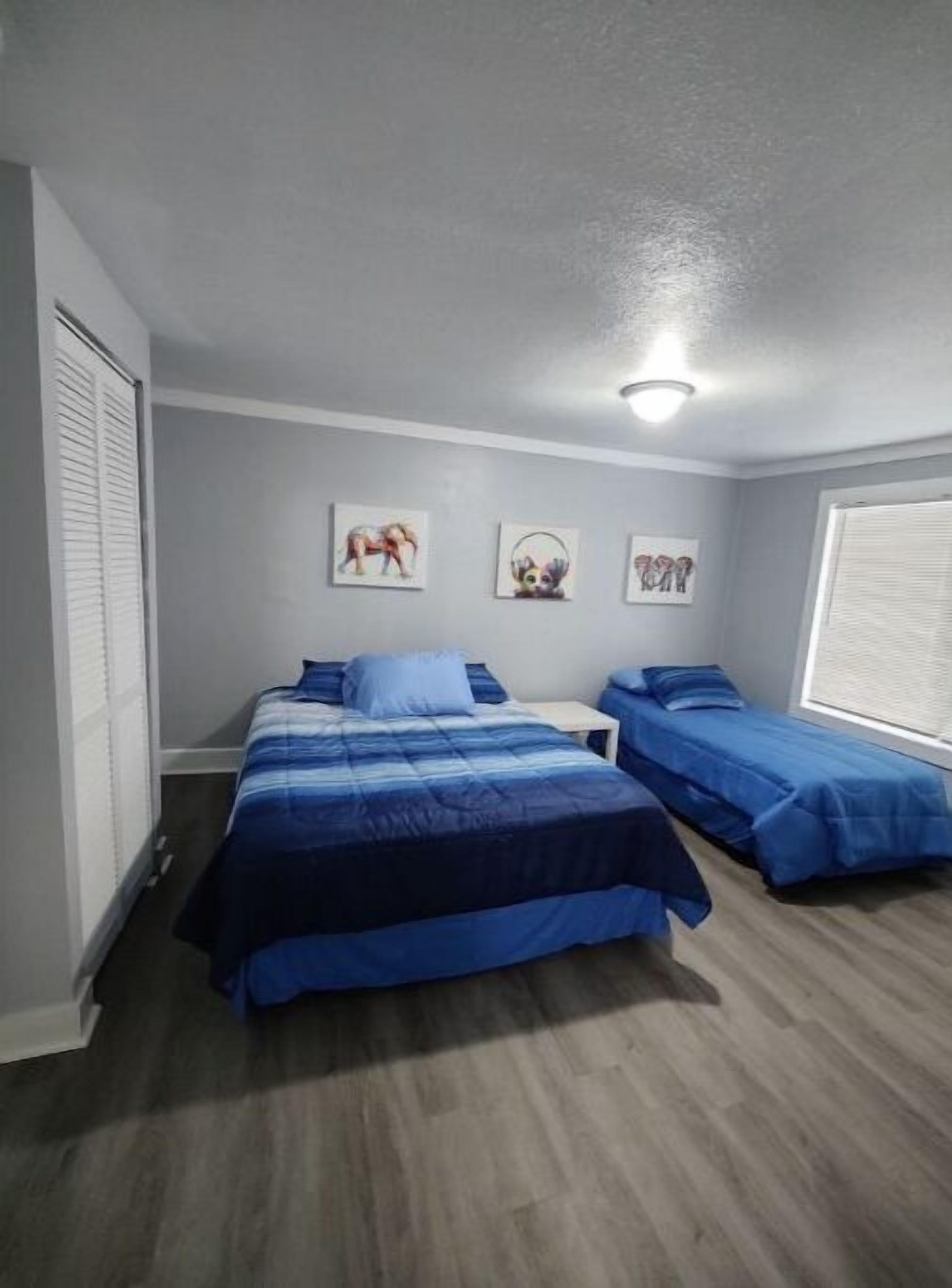 A bedroom with two beds, a window, and artwork on the wall.