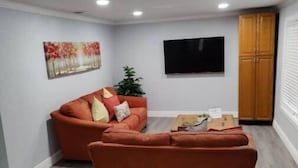 Ein Wohnzimmer mit zwei orangefarbenen Sofas, einem Flachbildfernseher und einem Holzkabinett.
