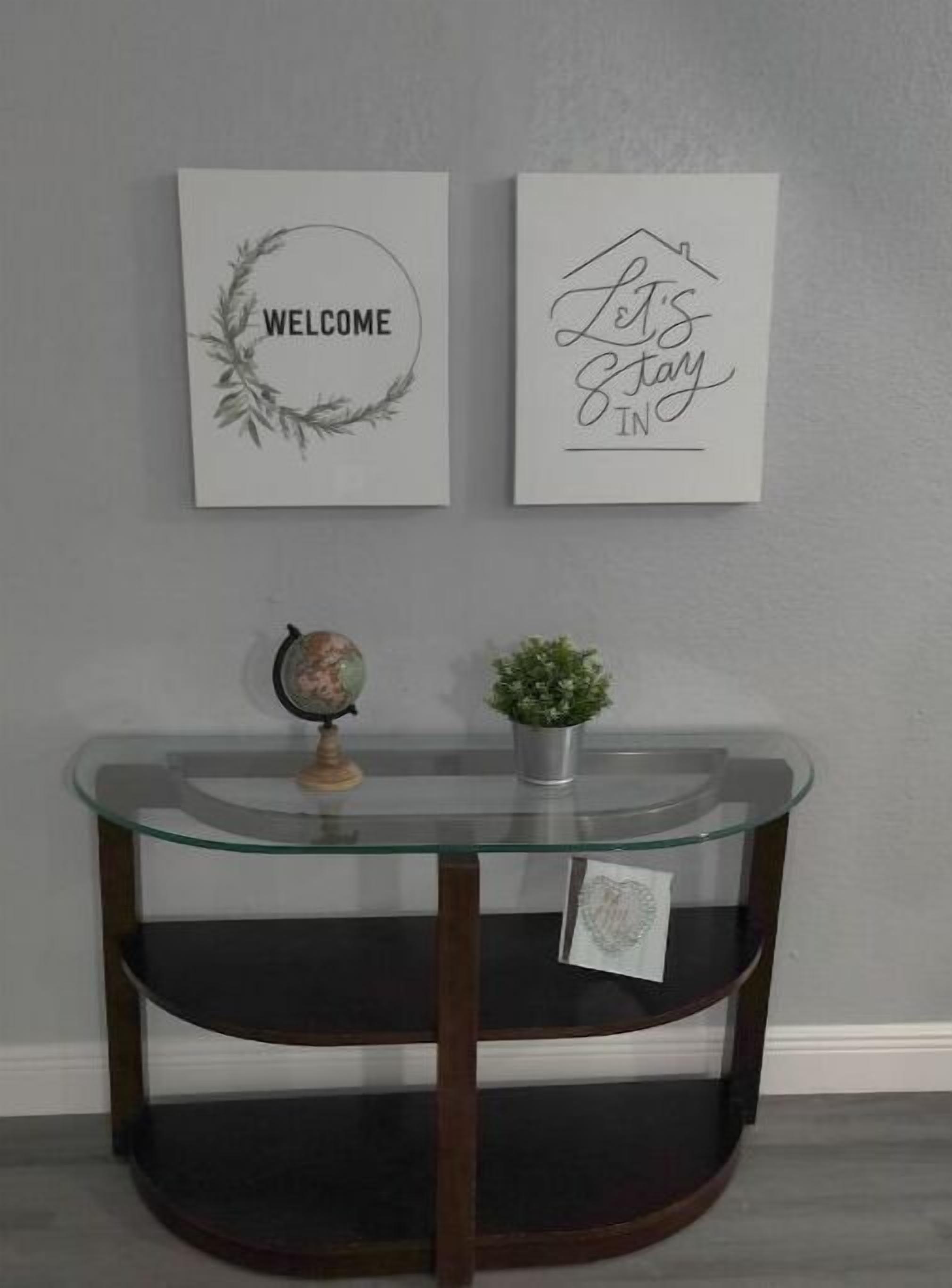 A glass-top table with a globe and a small plant, flanked by two framed signs reading "WELCOME" and "Let's Stay In".