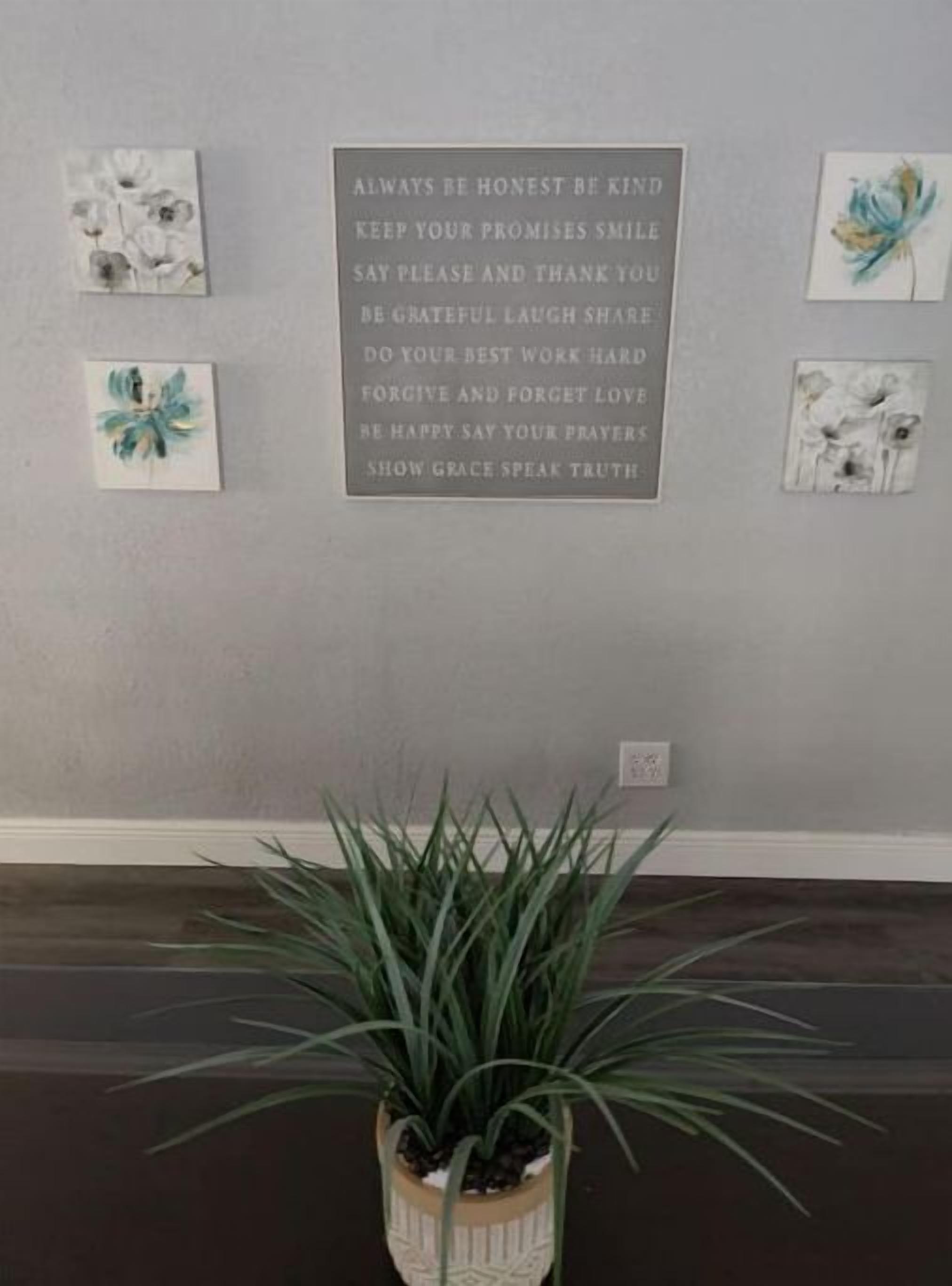 Una pared con una cita motivacional y cuatro obras de arte con motivos florales enmarcadas.