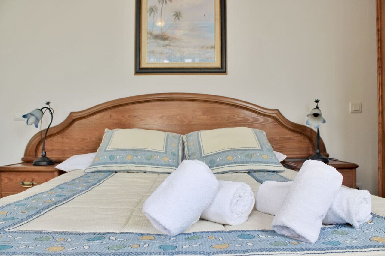 A neatly made bed with a blue and white patterned bedspread, two pillows, and two rolled white towels.