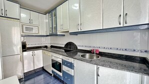 Una cocina compacta con armarios blancos, microondas, fregadero y estufa.