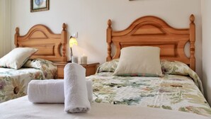 Habitación de hotel con dos camas de madera, ropa de cama floral, toallas blancas y cuadros en la pared.
