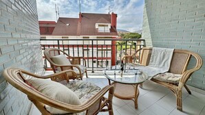 Un balcón con mobiliario de mimbre, una mesa de vidrio y vistas a un edificio con tejado rojo.
