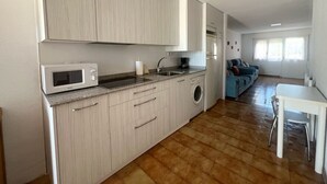 A compact kitchen with a microwave, sink, and washing machine, leading to a living area with a sofa and a dining table. - Casa Rural Con Jardín Y Barbacoa - A Babor 20805 (Cantabria)