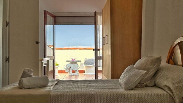 A bedroom with a bed, a wooden door, and a view of an outdoor patio with a table and chairs. - Casa Rural Con Jardín Y Barbacoa - A Babor 20805 (Cantabria)