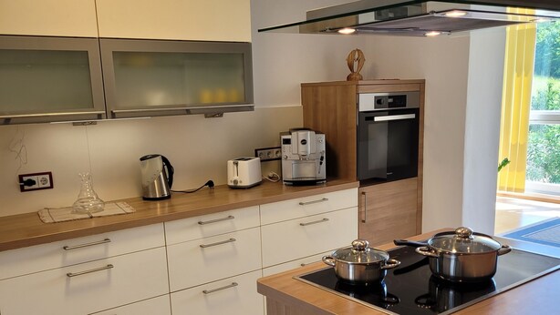 Una cocina moderna con armarios blancos, encimera de madera, estufa integrada y cafetera.