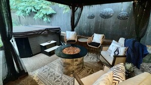 Un'area patio coperta con un braciere in pietra, posti a sedere all'aperto e una vasca idromassaggio.