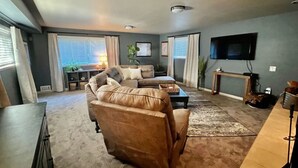 A living room with a sectional sofa, a coffee table, a flat-screen TV, and a fireplace. - Moody Country Farmhouse (Albany)