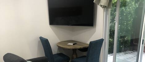 A modern room with a sofa, a small table, and chairs. A flat-screen TV is mounted on the wall.