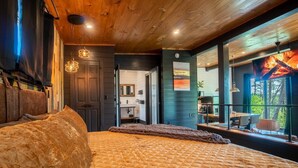 A bedroom with a large bed, a wooden ceiling, and a view of the outdoors.