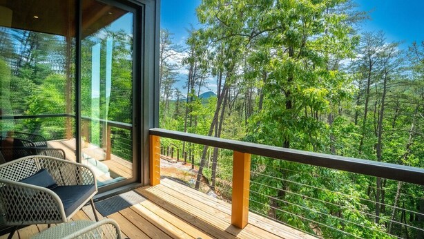 A balcony with a wooden deck, wicker chairs, and a view of a forested area.
