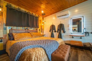 Um quarto aconchegante com uma cama grande, um banquinho, um porta-robes e um espelho.