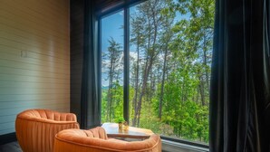 A room with two orange chairs, a small table, and a large window offering a view of a forest.