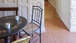 A room with a rustic stone wall, a wooden door, a round table with two white mugs, a wicker chair, and a hallway leading to another room. - La Maison de L'amiral (Moëlan-sur-Mer)